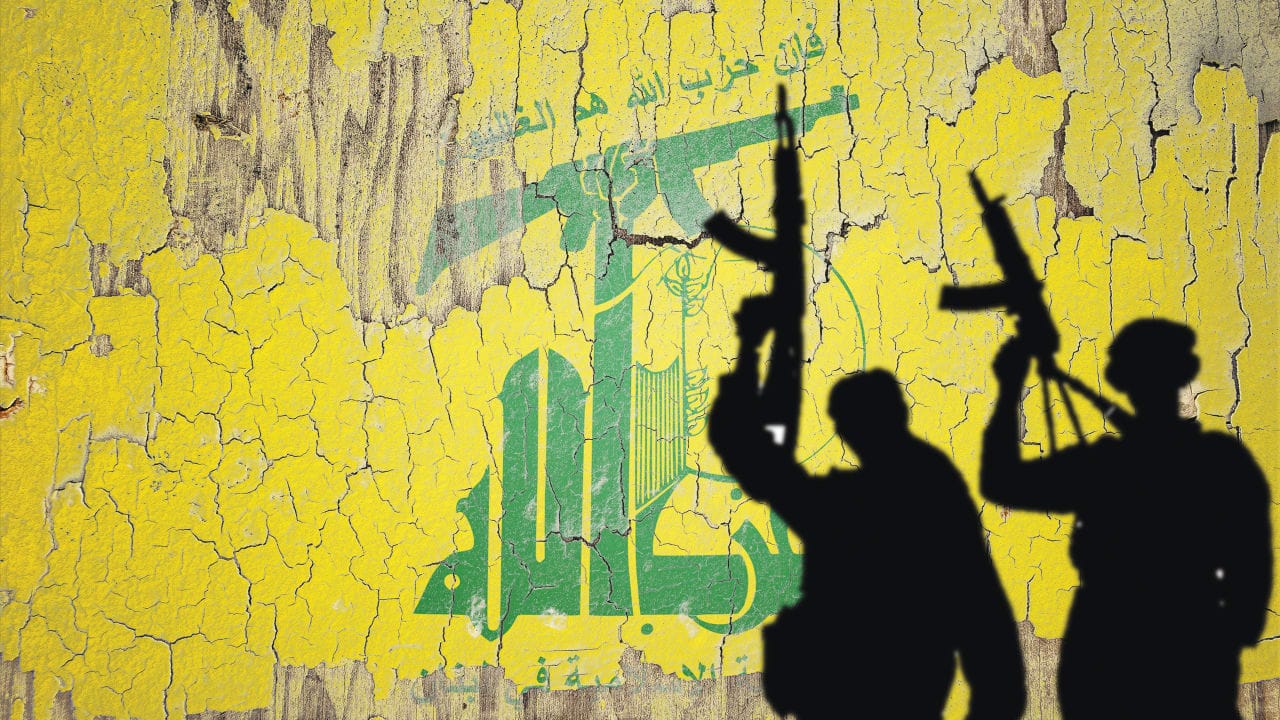 Hezbollah flag mural provides backdrop for gun-wielding shadows.