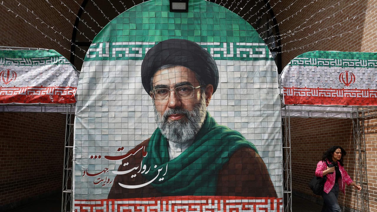 A woman walks next to a banner with a picture of Iran's new Supreme Leader Mojtaba Khamenei in Tehran, Iran, May 8, 2026. 