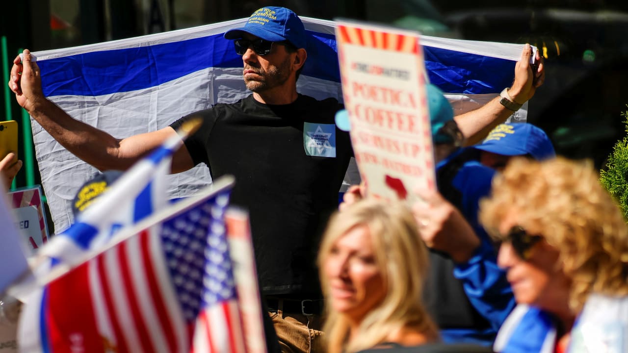 A demonstrator holds an Israeli flag as protesters gather during an '#EndJewHatred' rally outside Poetica Coffee, following a social media post by the shop targeting Jewish Congressman Dan Goldman and denying service to pro‑Israel customers in Brooklyn, New York.