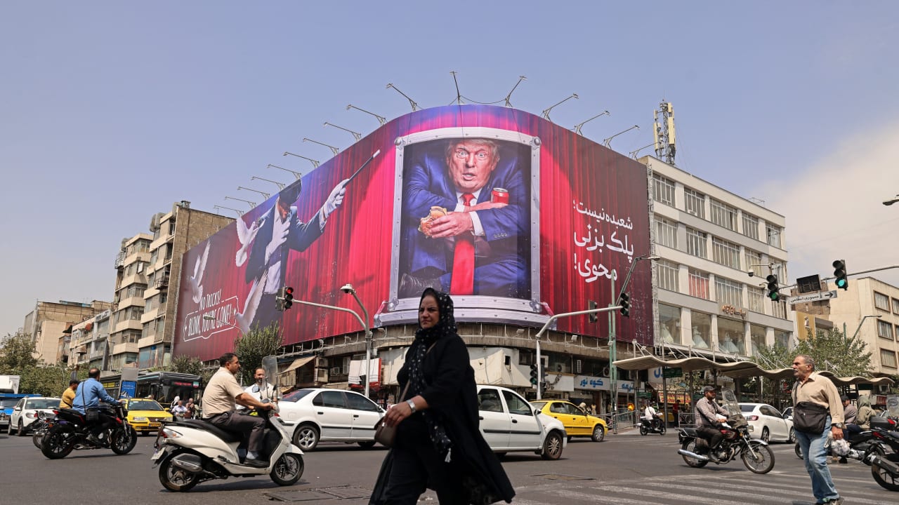 A pedestrian walks past a billboard depicting US President Donald Trump inside a catering container, installed on a building along a street in downtown of Tehran on August 31, 2026.