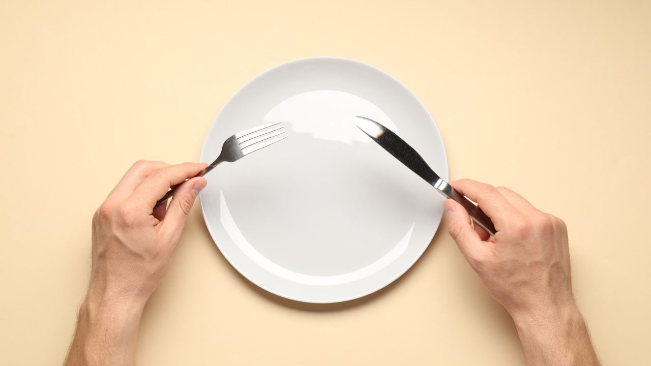 Man with cutlery and plate on beige background.