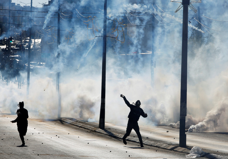 Palestinian protestors hurl stones as tear gas is fired by Israeli troops during clashes following President Trump's announcements surrounding Jerusalem (credit: Mussa Qawasma/ Reuters)