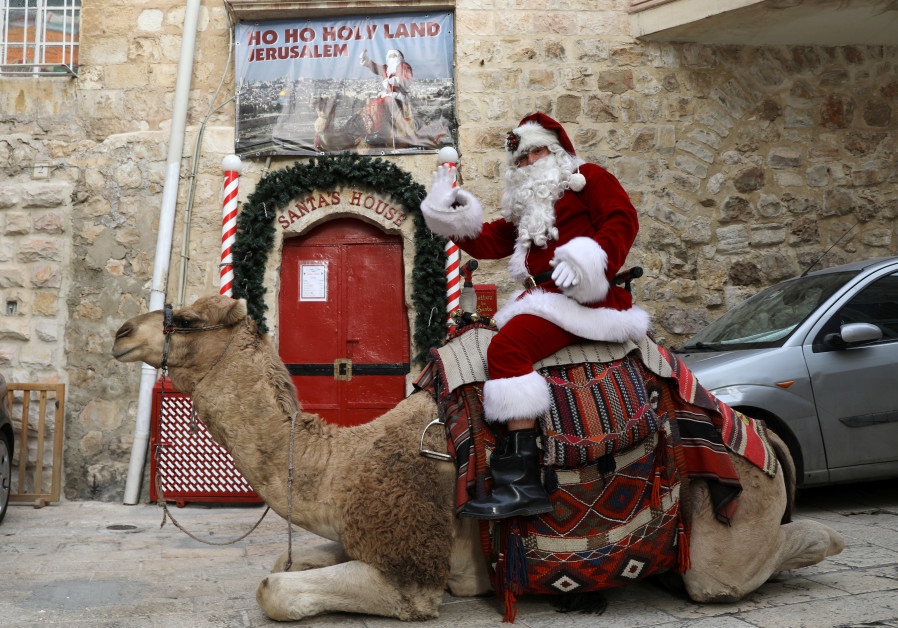 Issa Kassissieh rides a camel in a Santa costume during the annual Christmas tree distribution in the Old City of Jerusalem (credit: Ammar Awad/ Reuters)