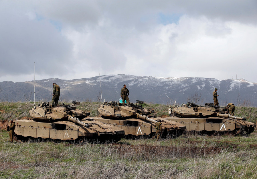 Israeli soldiers stand atop tanks overlooking the border between Israel and Syria