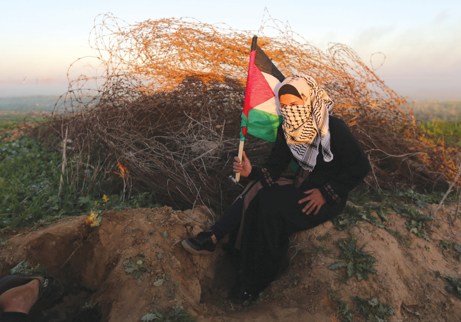 Une PALESTINIENNE se met à l'abri lors d'une manifestation vendredi à la barrière de protection entre Israël et Gaza