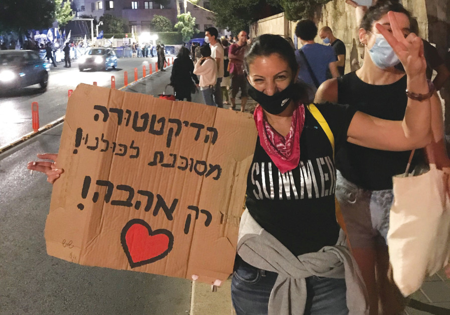GILAT OF Ganei Tikva, pink bandana around her neck, displays a sign reading, ‘The dictatorship is a danger to all of us! Only love!’ in front of the residence. (Credit: Sarah Levi)