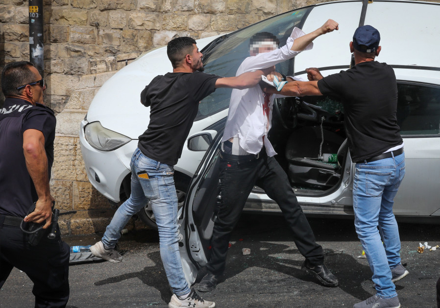 An Israeli police officer runs to rescue an injured Jewish man after his car swerved off road near Jerusalem's Old City after it was pelted by rocks on May 10, 2021 (Credit: OLIVIER FITOUSSI/FLASH90)