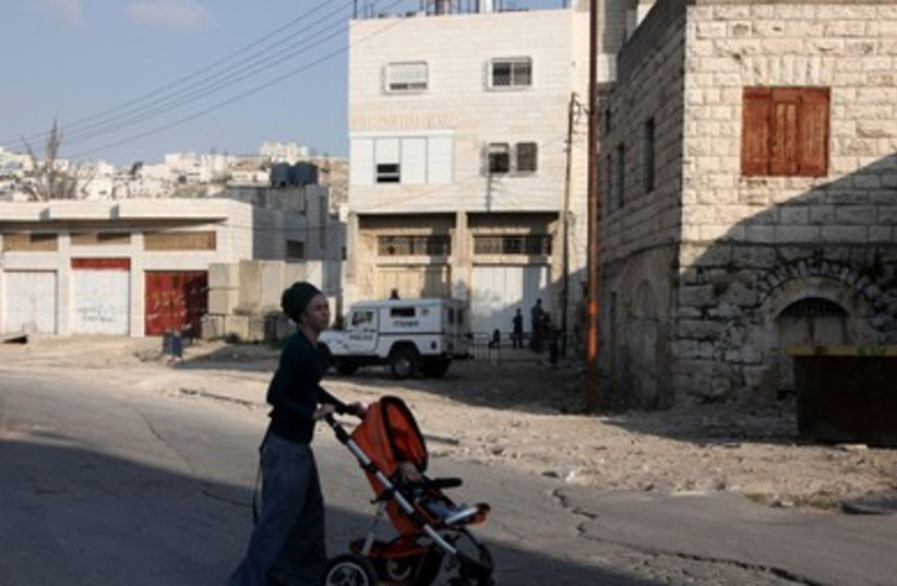 A Jewish woman wheels her child by the Hebron home