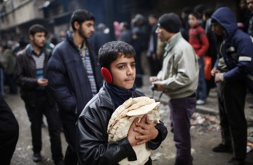 Boy holds bread as others line up outside bakery in Aleppo 3 (photo credit: reuters)