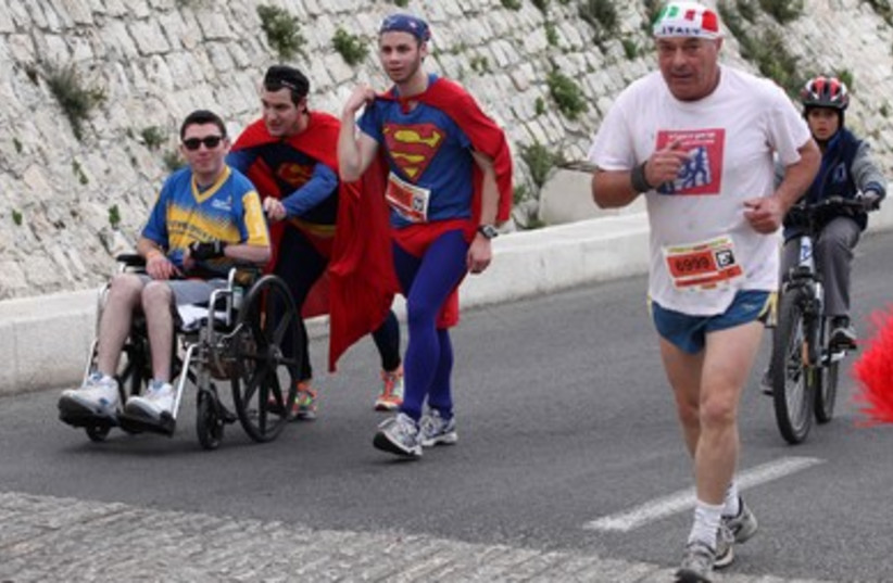 Man dressed as superman pushes a competitor doing the marathon in a weelchair 