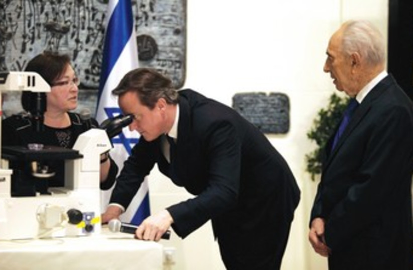 British Prime Minister David Cameron looks through a microscope at regenerating cells, part of a Parkinson’s disease research project. (photo credit: REUTERS)