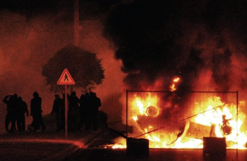 Young residents of Villiers-le-Bel, a northern Paris suburb, vandalize an abandoned police car during clashes, November 26, 2007, the second night of street violence after two local teens were killed in a crash with a police patrol car (photo credit: ALEXANDRE GUY / ABACA PRESS / MCT)