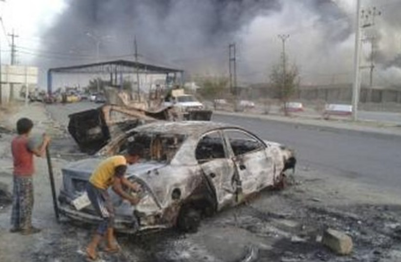 Civilian children stand next to a burnt vehicle during clashes between Iraqi security forces and al Qaeda-linked Islamic State in Iraq and the Levant (ISIL) in the northern Iraq city of Mosul, June 10, 2014.  (photo credit: REUTERS)