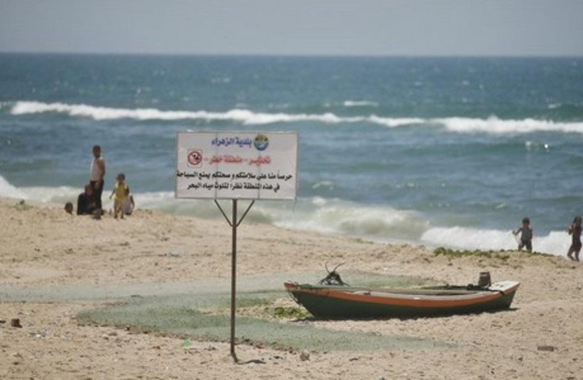 Palestinian children swim where sign warns against swimming on a beach in Gaza  (photo credit: REUTERS)