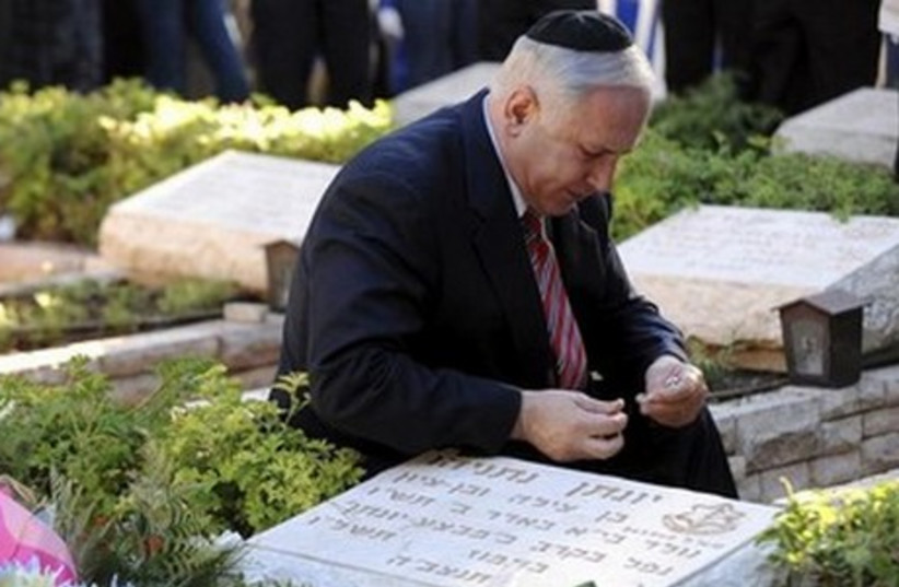 Prime Minister Binyamin Netanyahu kneels at the gravesite of his brother, Yoni Netanyahu. (photo credit: REUTERS)