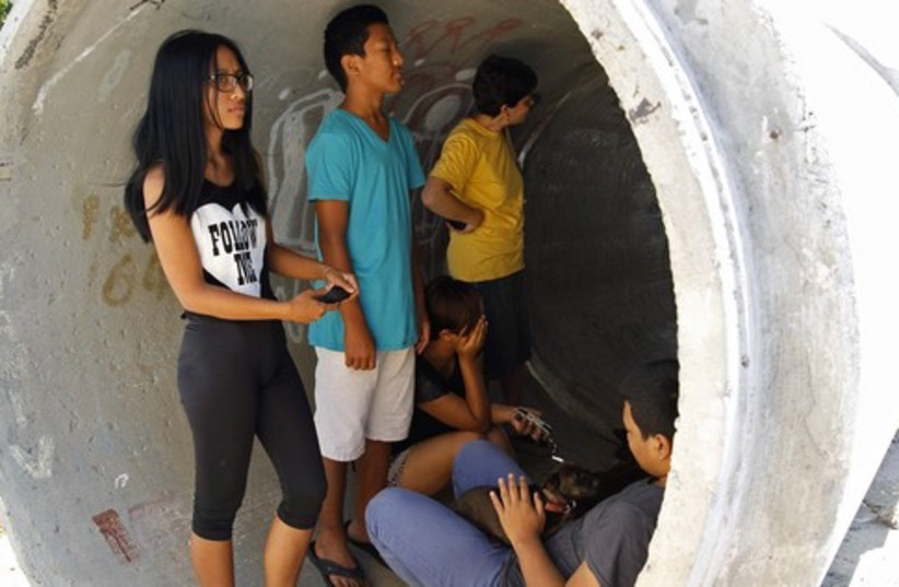 Residents take cover in a concrete pipe as a siren warning of incoming rockets is sounded near Ashdod (photo credit: REUTERS)