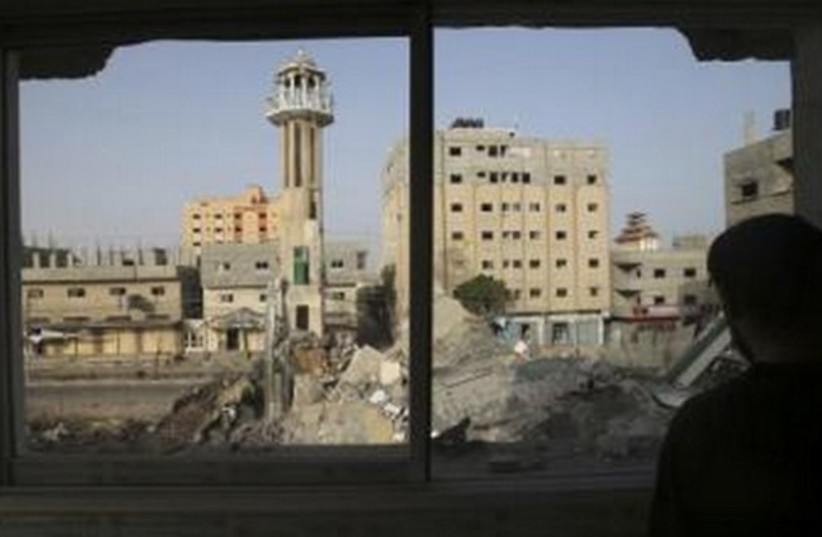 A Palestinian man looks through a broken window in the Gaza Strip, which police said was destroyed in an IAF strike. (photo credit: REUTERS)
