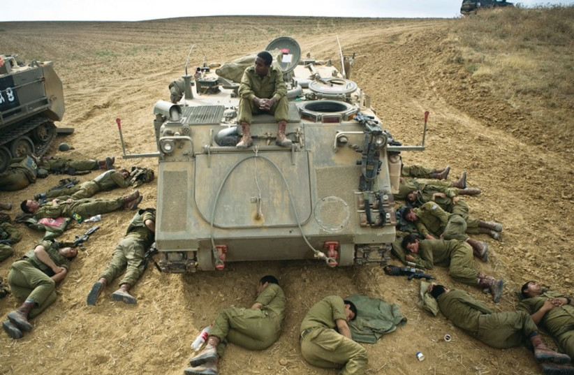 IDF SOLDIERS sleep on the ground next to an armored personnel carrier outside the Gaza Strip. (photo credit: REUTERS)