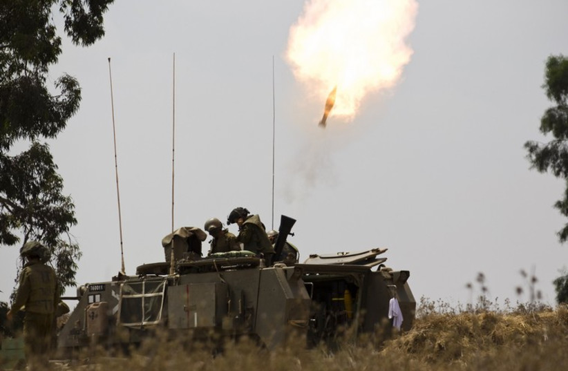 An Israeli soldier sits atop a mobile artillery unit in a staging area outside the Gaza Strip (photo credit: REUTERS)