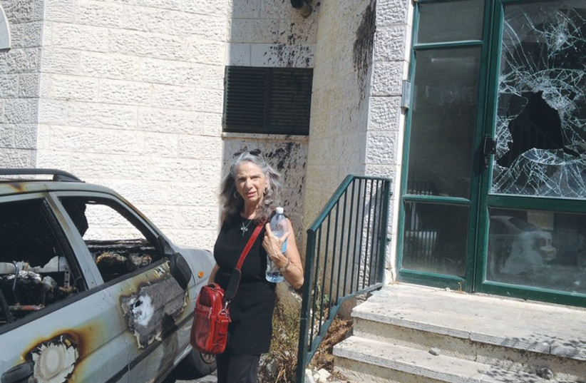 ABU TOR resident Bonnie Brooks stands between a car that was firebombed and the shattered entrance to a building (photo credit: DANIEL K. EISENBUD)