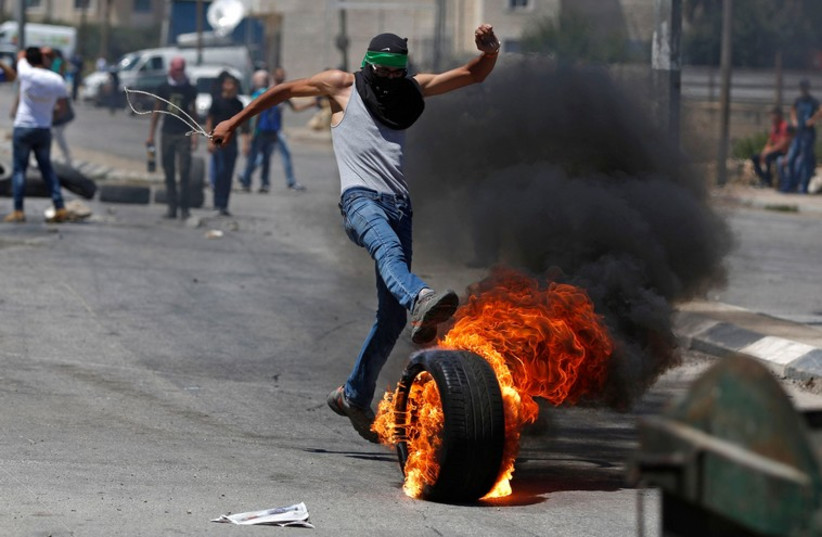 A Palestinian protester kicks a burning tire during clashes with Israeli troops at a protest in West Bank city of Ramallah (photo credit: REUTERS)
