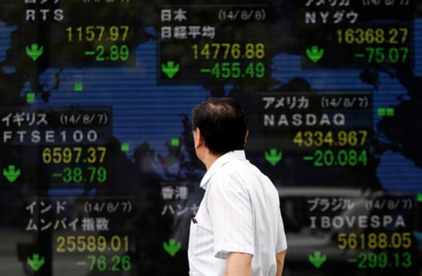 A pedestrian looks at an electronic board showing the stock market indices of various countries outside a brokerage in Tokyo. (photo credit: REUTERS)
