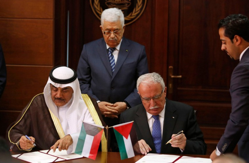 Kuwait's Minister of Foreign Affairs and Palestinian Foreign Minister Riyad al-Malki sign a memorandum of understanding as PA President Abbas stands behind them in Ramallah September 14 (photo credit: REUTERS)