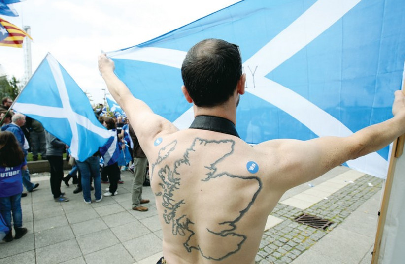 A MAN with a tattoo of Scotland on his back holds up a Scottish flag to support independence at a rally in Glasgow. (photo credit: REUTERS)