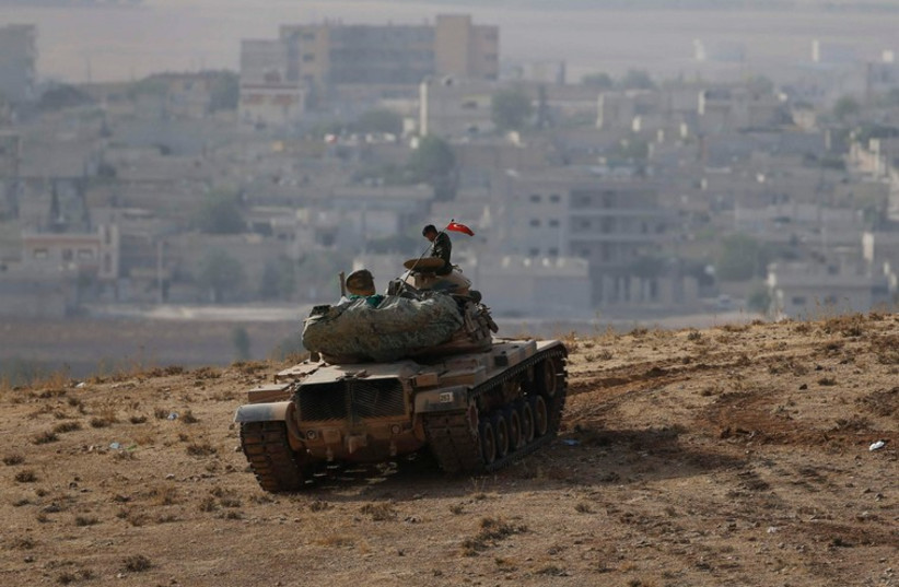 A Turkish soldier sits on top of a tank, with the Syrian town of Kobani in the background. (photo credit: REUTERS)