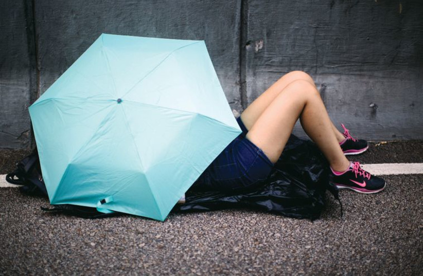 Illustrative: A woman sleeps under an umbrella in Hong Kong. (photo credit: REUTERS)
