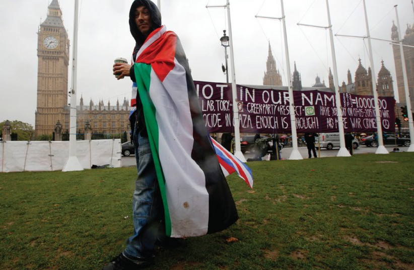 AN ACTIVIST wears a Palestinian/Union Jack flag outside the Houses of Parliament before Monday’s vote on Palestinian recognition. (photo credit: REUTERS)