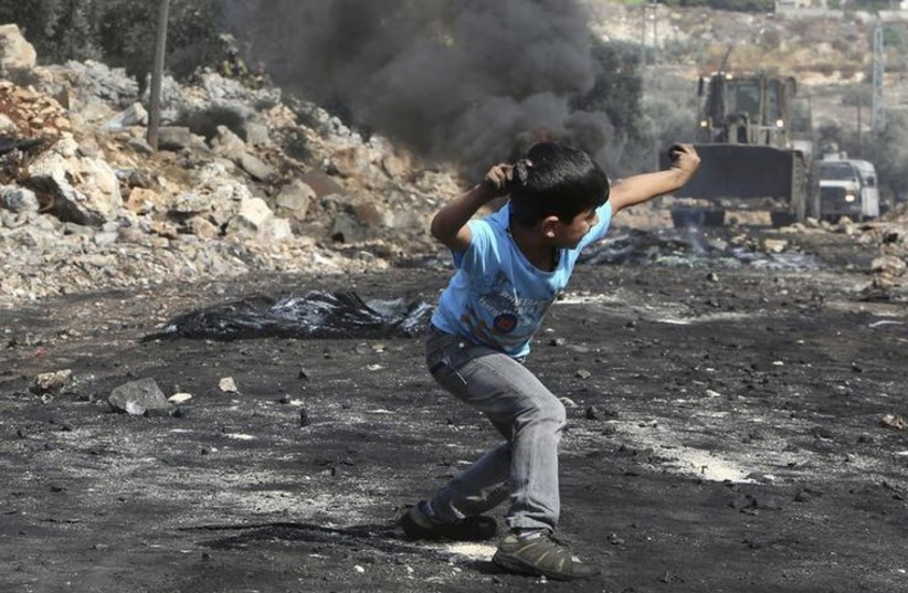 A Palestinian boy throws stones at an armored wheel loader of the Israel Defense Forces during clashes near Nablus (photo credit: REUTERS)