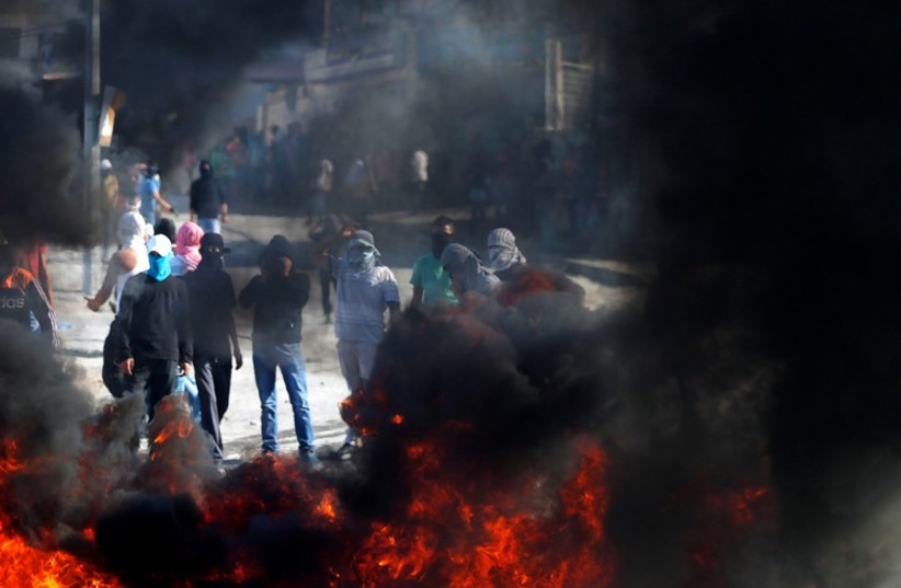 Masked Palestinian protesters stand near burning tyres during clashes with Israeli police, October 24 (photo credit: REUTERS)