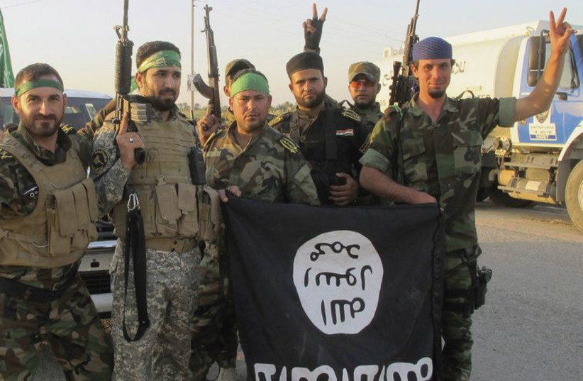 Shi’ite fighters pose with a black flag belonging to the Islamic State. (photo credit: REUTERS)