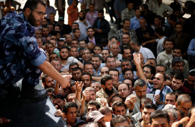 A Palestinian policeman gestures as Hamas-hired civil servants wait to receive a payment in Gaza City (photo credit: REUTERS)