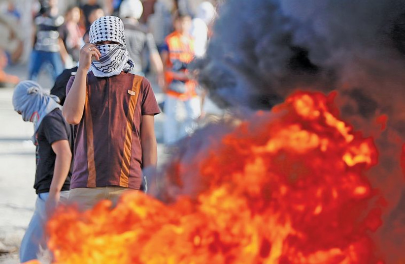 A masked Palestinian protester stands near burning tires during clashes with police in Isawiya. (photo credit: REUTERS)