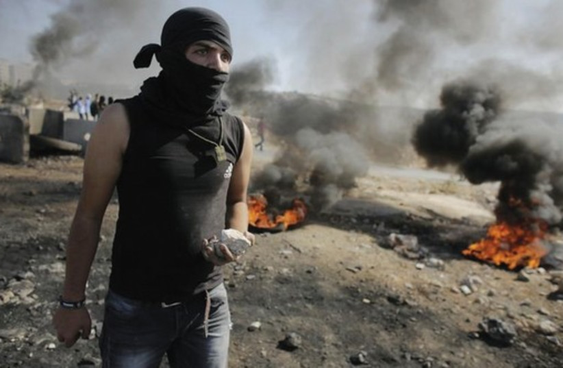 Youth holds stone as Palestinians clash with IDF in the West Bank (photo credit: REUTERS)