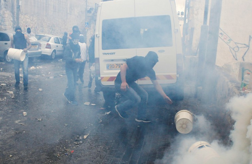 ARAB YOUTHS try to prevent a tear gas canister from emitting more gas during a confrontation with police in the capital’s Abu Tor neighborhood (photo credit: REUTERS)