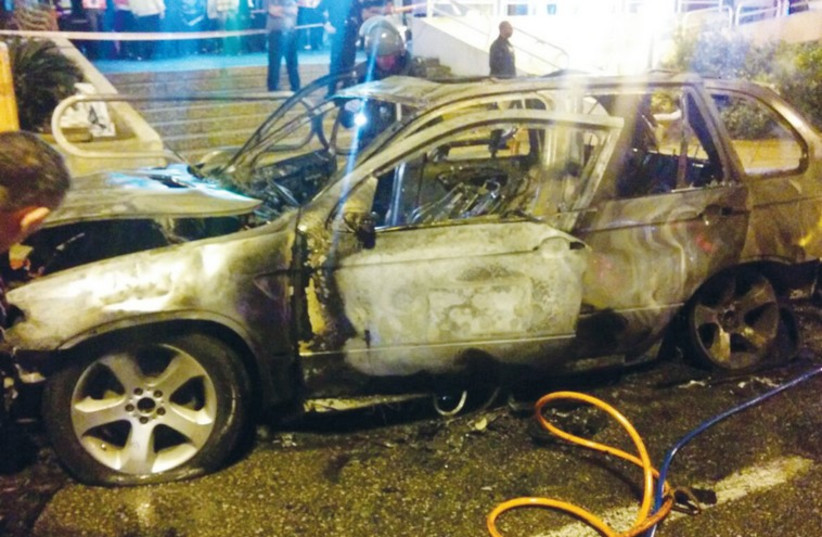 Bystanders look from a distance at the remains of a car that exploded in Ashdod, November 4 (photo credit: ISRAEL POLICE)