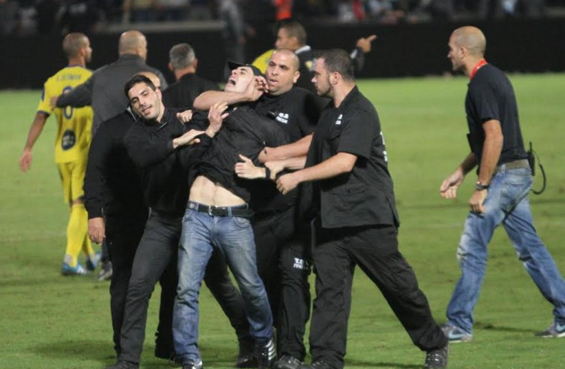 Security guards haul away a fan who ran onto the pitch (photo credit: ADI AVISHAI)