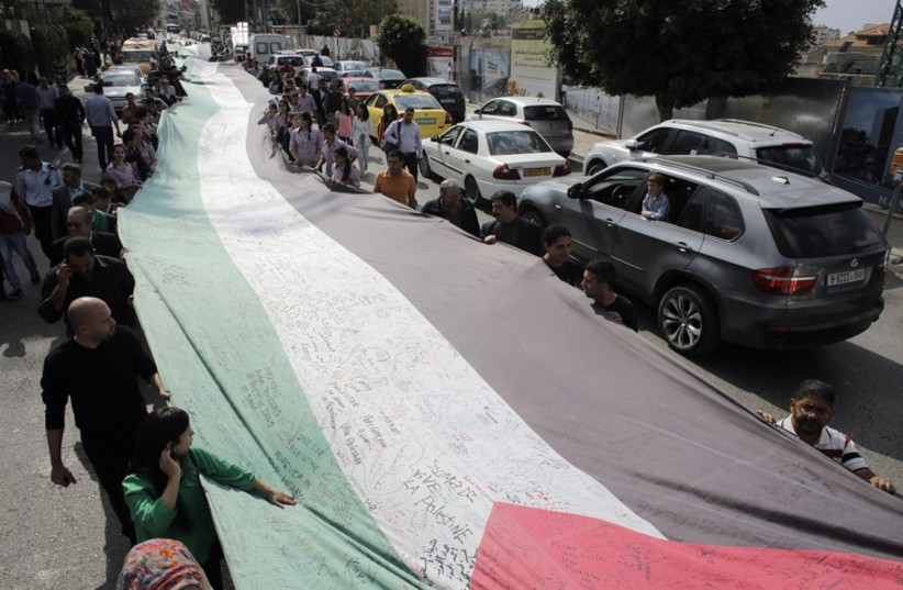 PEOPLE MARCH as they hold a large Palestinian flag in Ramallah in October (photo credit: REUTERS)