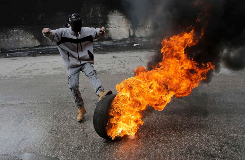 A Palestinian protester kicks a burning tyre during clashes with Israeli troops near Israel's controversial barrier  (photo credit: REUTERS)
