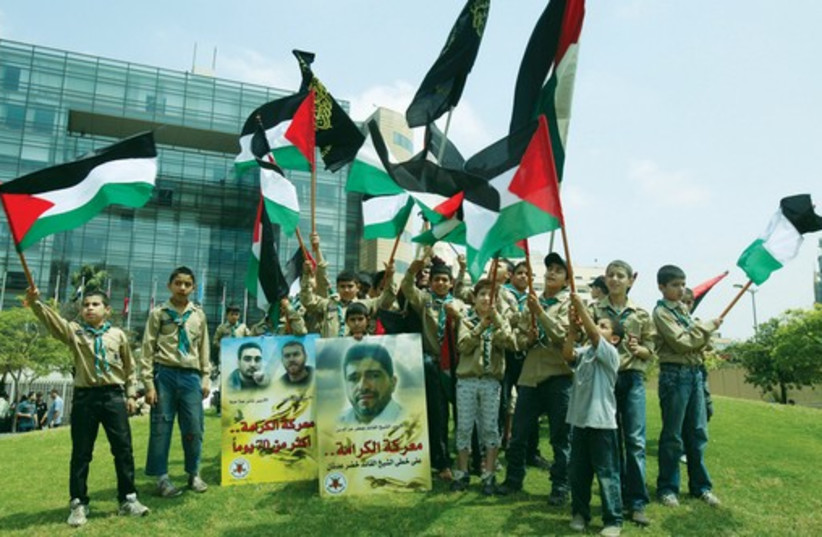 Palestinian members of a youth group wave their national flags and hold posters depicting portraits of Palestinian prisoners during a protest in solidarity with them. (photo credit: REUTERS)
