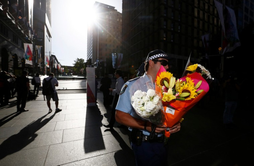 An Australian police officer carries a bouquet left as a floral tribute after the Sydney cafe siege ended December 16, 2014.  (photo credit: REUTERS)