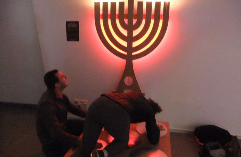 Adults play with a hanukkia that lights up when limbs used to make an electrical circuit.  (photo credit: JUDY SIEGEL-ITZKOVICH)