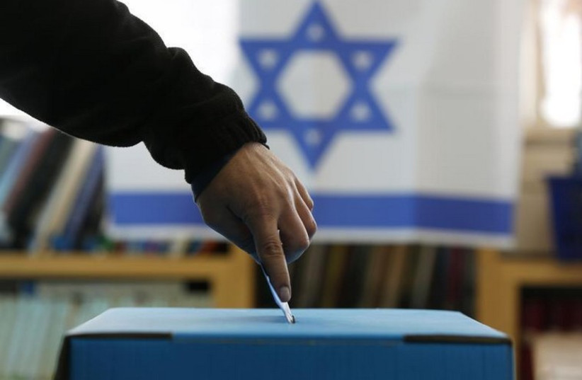 An Israeli flag is seen in the background as a man casts his ballot for the parliamentary election (photo credit: REUTERS)
