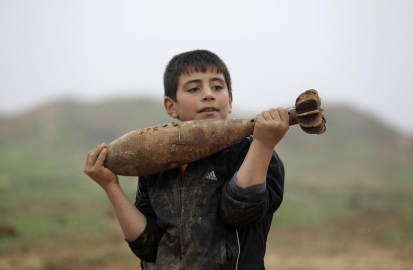 A boy carries a mortar shell left behind by forces loyal to Syria's President Bashar al-Assad at the Azaalana checkpoint (photo credit: REUTERS)