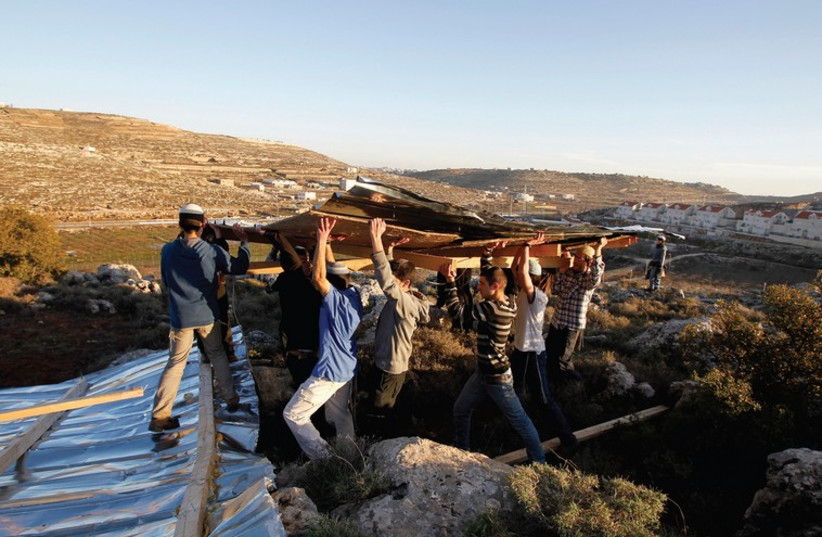 JEWISH MEN carry wooden planks as they build a makeshift structure at the unauthorised outpost of Mitzpe Avihai, also known as Hill 18, near Kiryat Arba outside the West Bank city of Hebron in 2012. (photo credit: REUTERS)