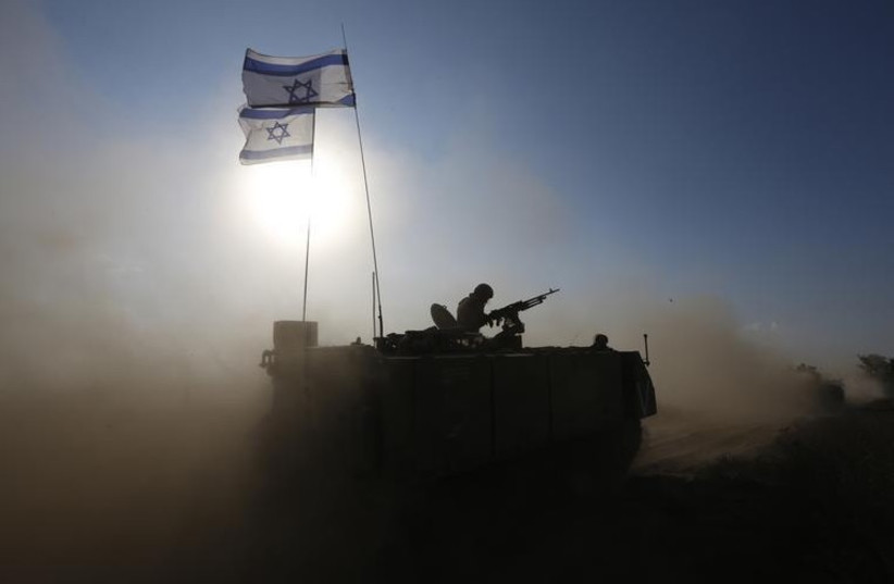 An IDF soldier rides an armored personnel carrier toward a staging area near the Gaza border (photo credit: REUTERS)