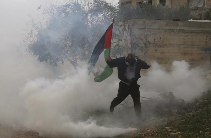 A Palestinian protester holding a Palestinian flag runs away from tear gas fired by Israeli soldiers during clashes following a protest against the nearby Jewish settlement of Qadomem (photo credit: REUTERS)